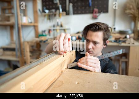 Woodshop employee working with old window frame parts at worktable in restoration workshop. Stock Photo