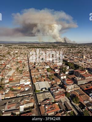 Aerial view of the Uruapan wildfire with a large plume of smoke rising over the city rooftops and surrounding hills, Uruapan, Michoacan, Mexico. Stock Photo