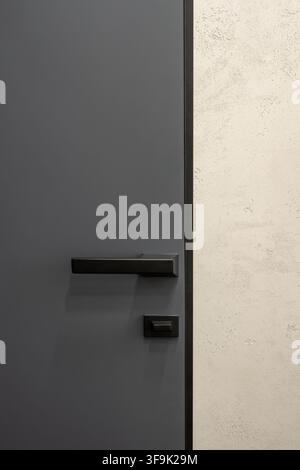 Minimalist modern interior door with matte dark gray finish and black rectangular lever handle, contrasting with textured light plaster wall Stock Photo