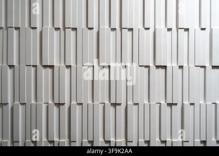 Contemporary white textured wall with geometric 3D panels arranged in a staggered vertical pattern, creating depth, shadows and a minimalist architect Stock Photo