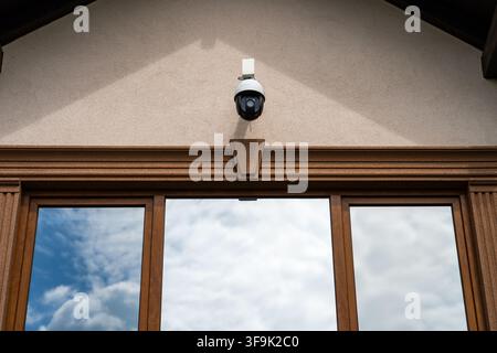 Outdoor security camera mounted above house windows reflecting cloudy sky, home surveillance system Stock Photo
