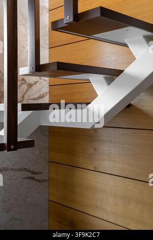 Close-up of modern floating wooden staircase steps with white metal frame, luxury interior architecture detail Stock Photo