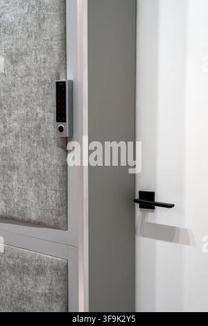 Modern interior door with smart electronic keypad lock and black lever handle, minimalist gray and white design with upholstered wall panels Stock Photo