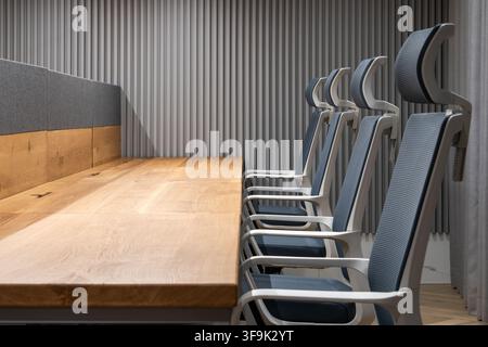 Contemporary office interior featuring ergonomic conference chairs arranged along a wooden meeting table, acoustic slat wall and minimalist wall light Stock Photo