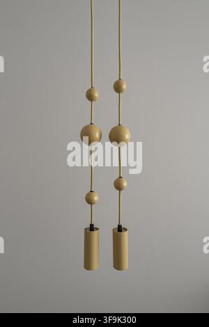Minimalist modern pendant lights with brass cylindrical shades and spherical decorative elements suspended from thin cords against a neutral gray wall Stock Photo