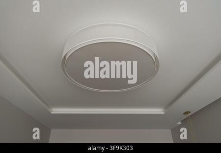 Minimalist modern ceiling with a large round flush mount light fixture and recessed perimeter lighting in an elegant contemporary interior Stock Photo
