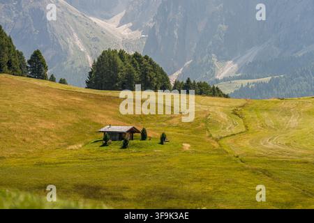 Small wooden alpine hut in a sunny meadow beneath the Dolomite mountains in Italy Stock Photo
