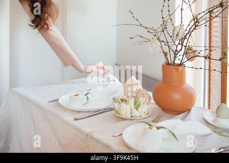 Dining table beautifully arranged with decorative plates, spring flowers, and a vase with branches and eggs, creating a festive atmosphere in a bright Stock Photo