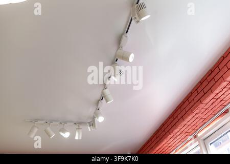 Ceiling-mounted track lighting with multiple adjustable spotlights illuminating a modern interior space with a red brick wall Stock Photo