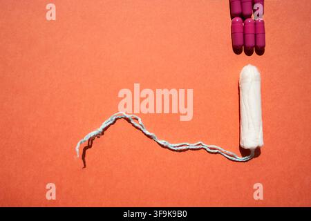 Tampon with a blue string positioned on an orange surface next to purple capsules, representing feminine hygiene products and health-related themes Stock Photo