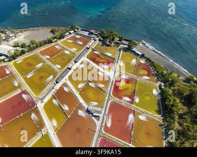 Aerial view of a shrimp farm with rectangular ponds showing shades of orange and red water, aerators creating white splashes, along the coast in Kecam Stock Photo