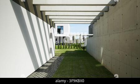 Modern concrete and white architectural structure with geometric shadows defining a walkway and green lawn Stock Photo