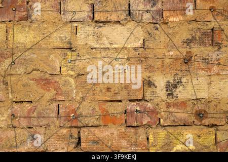 Detailed close-up of a weathered brick wall featuring a network of thin, dark wires. The bricks show various colors and imperfections, creating an abs Stock Photo
