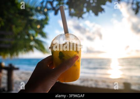 Hand holding a tropical fruit drink on a sunny beach in Maldives Stock Photo