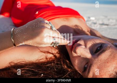 Woman in scarlet dress rests on sandy beach in Maldives Stock Photo