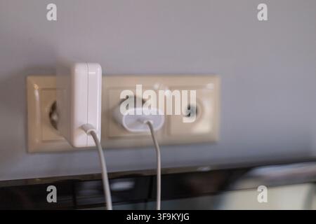 Two white power adapters and charging cables plugged into electrical wall sockets indoors, providing power supply to electronic devices. Stock Photo