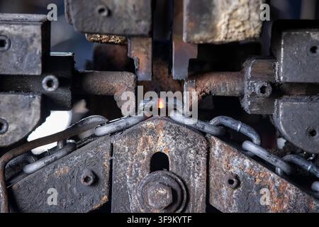 Hot Metal Chain Link Welding in Industrial Machine, Sparks and Glowing Steel During Heavy Manufacturing and Metalworking Process Stock Photo