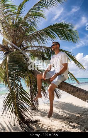 A man sits on a leaning palm tree along a tropical beach in Maldives Stock Photo