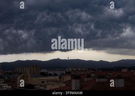 Dark and dramatic storm clouds gather above Barcelona and the Collserola mountain ridge, with the urban skyline and rooftops visible in the foreground Stock Photo