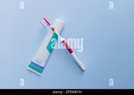Minimalist flat lay of a red and white manual toothbrush and a tube of toothpaste, arranged as a cross on a clean light blue surface Stock Photo