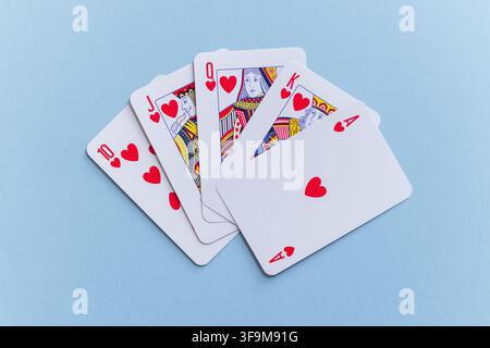 Royal flush hand of heart playing cards fanned out on a pastel light blue background. Minimalist flat lay stock photo representing luck, victory, casi Stock Photo