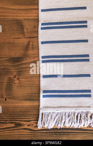 Detailed top view of a white woven cotton rug with blue stripes and fringe lying on a dark rustic wooden plank floor with empty copy space. Stock Photo