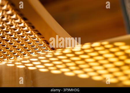 Close up view of natural woven rattan cane webbing casting a bright geometric shadow pattern onto a smooth wooden surface in warm sunlight. Stock Photo