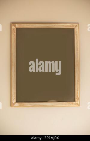 Vertical light wooden frame with empty blank dark copy space hanging on a plain neutral beige wall for artwork poster mockup display. Stock Photo