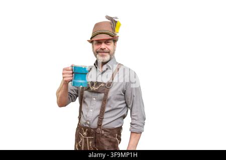 A smiling mature man in Bavarian clothing holds a blue mug against white. Stock Photo