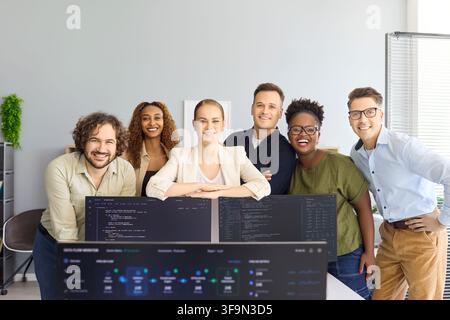 Smiling software team portrait behind monitors in contemporary startup office Stock Photo