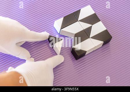 Conceptual image of machine learning. Hands in white gloves precisely assembling black and white geometric cubes. Creating complex patterns on a purpl Stock Photo