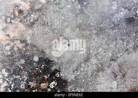 Close up of an abstract painted canvas showing layered grey, brown and white pigment with splatters, blotches and visible weave texture. Stock Photo