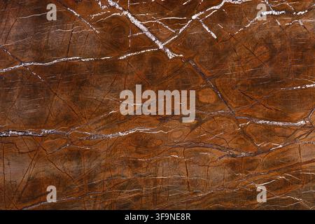 Full frame close up of a polished brown marble slab with branching white and dark veins running across warm rust and amber toned natural stone. Stock Photo