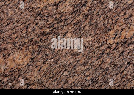 Full frame close up of a polished granite slab in warm brown tones, showing diagonal dark veining and crystalline speckles across the natural stone su Stock Photo