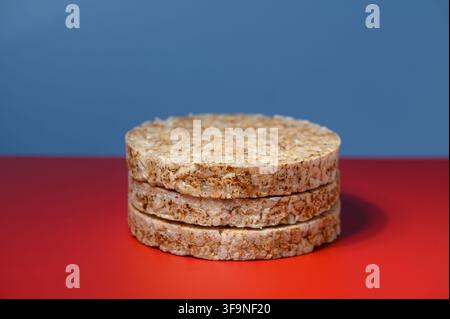 A studio photograph featuring a neat stack of round, grainy rice cakes set on a vivid red surface against a smooth blue gradient background. Stock Photo