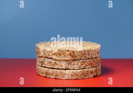 A studio photograph featuring a neat stack of round, grainy rice cakes set on a vivid red tabletop against a smooth blue gradient background, captured Stock Photo