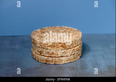 A studio photograph featuring a neat stack of round, grainy rice cakes set on a dark textured surface against a smooth blue gradient background. Stock Photo
