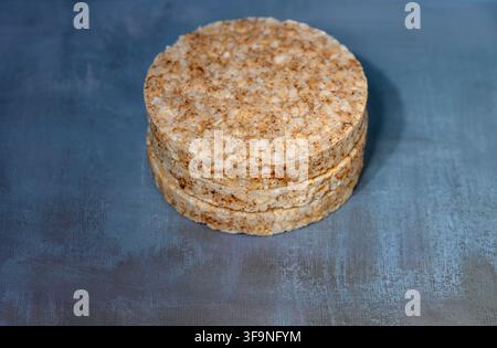 A studio photograph showcasing a stack of round, grainy rice cakes positioned on a textured blue-grey surface with soft lighting and shadows. Stock Photo