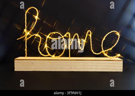 Glowing home word made of warm fairy lights on wooden base against black background for cozy interior decor or housewarming design Stock Photo