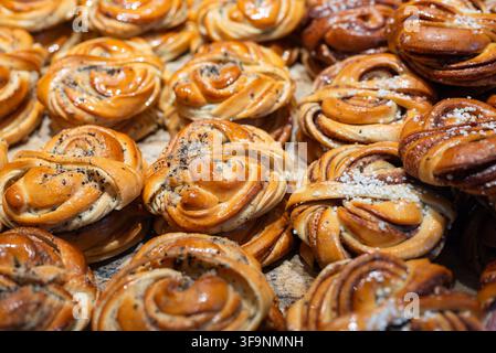 Traditional Swedish cinnamon and cardamom buns with twisted dough, sugar topping and glossy baked crust, displayed fresh in a bakery. Stock Photo
