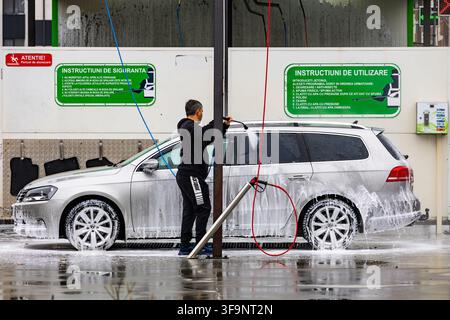 Bucharest, Romania - April 20, 2026: Man washing silver station wagon car covered in active soap foam at self service car wash station Stock Photo