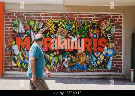 People walking past colourful graffiti street art with Marmaris sign painted on a brick wall background in resort town Marmaris, Turkey Stock Photo