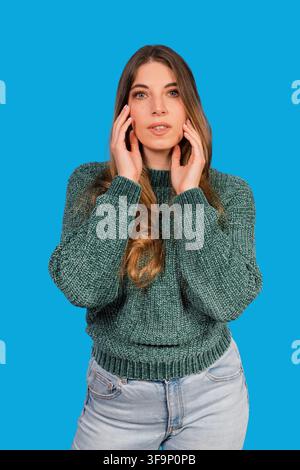 Young woman touching her face with both hands, expressing thoughtfulness Stock Photo