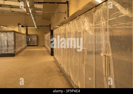 Rows of Brand New Glass Door Commercial Refrigerator Cabinets Covered in Protective Plastic Film Inside Unfinished Supermarket Under Construction Stock Photo