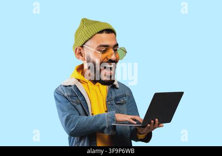 Happy Young Latin American Man Using Laptop, Smiling And Enjoying At Home, Technology Concept Stock Photo