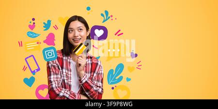 Smiling Young Asian Woman Holding Credit Card In Front Of Colorful Social Media Icons, Business Concept Stock Photo