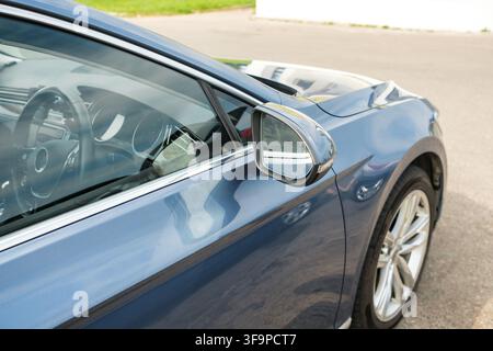 Close-up view of a blue car side mirror reflecting the surroundings, showcasing the sleek design and shiny finish of the vehicle Stock Photo