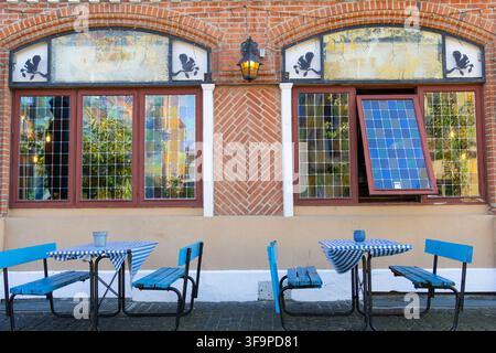 Outdoor cafe seating in Aalborg, Denmark, with blue tables and benches in front of a brick building with stained glass windows and one open window, cr Stock Photo