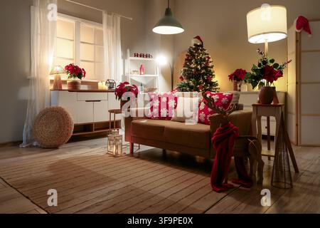Cozy living room decorated for christmas with a festive tree poinsettias and warm lighting creating a welcoming holiday atmosphere Stock Photo