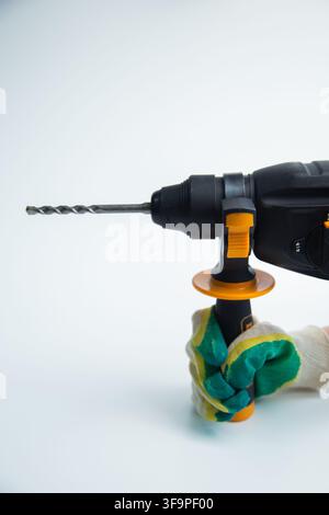 A gloved hand holds the black rotary hammer assist handle with orange accents and a drill bit firmly Stock Photo